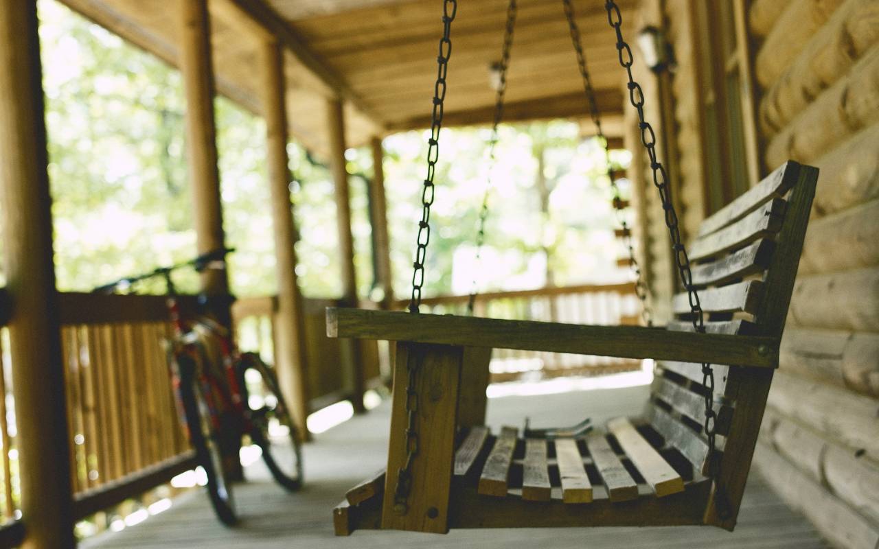 A wooden porch swing hangs in front of a wooden home.