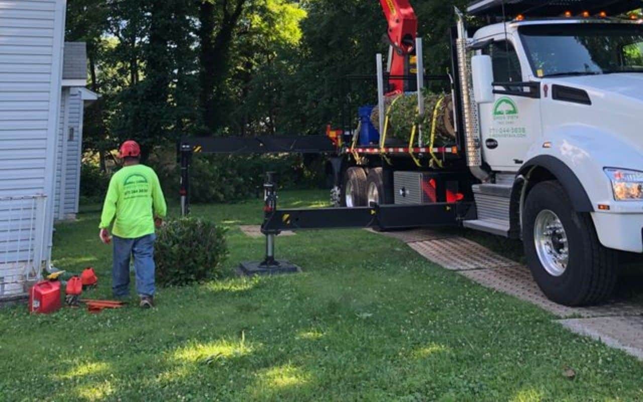 A tree removal crane works over a lawn that is covered with ground protection mats beneath its outriggers and tires.