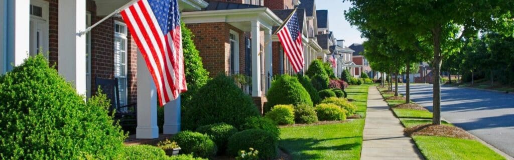 Mature street trees line the sidewalk in front of brick homes in an established Northern Virginia neighborhood.